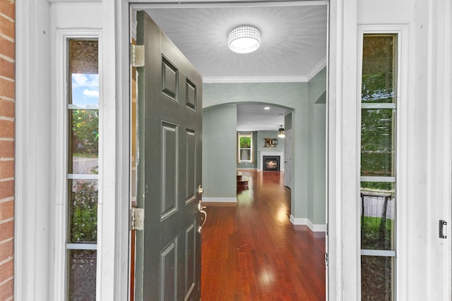 entryway with arched walkways, dark wood-type flooring, ornamental molding, baseboards, and a lit fireplace