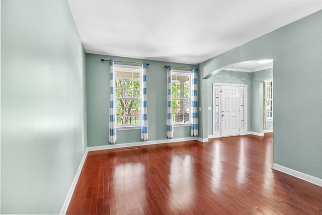 spare room with arched walkways, baseboards, and wood finished floors