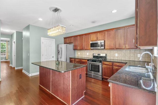 kitchen with appliances with stainless steel finishes, a sink, a kitchen island, baseboards, and dark stone countertops