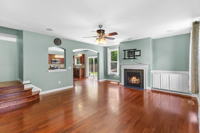 unfurnished living room with ceiling fan, a fireplace with flush hearth, arched walkways, and wood finished floors