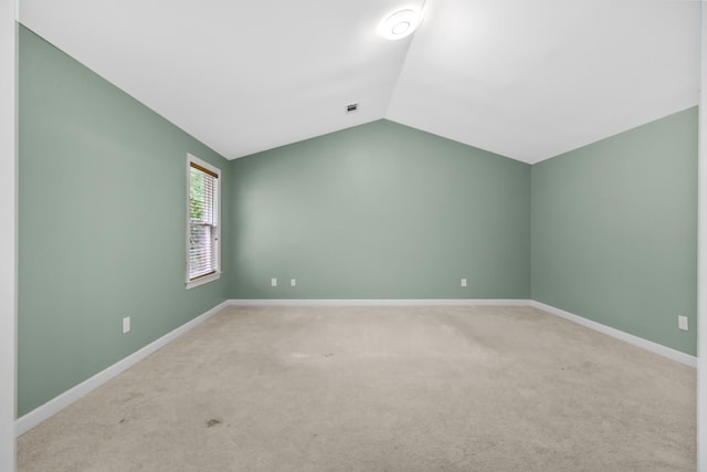 spare room featuring lofted ceiling, carpet flooring, and baseboards