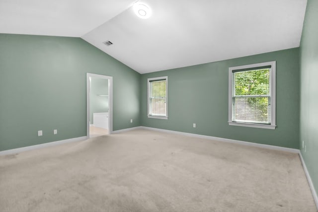 unfurnished bedroom with vaulted ceiling, light carpet, baseboards, and ensuite bathroom