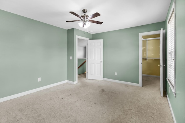 unfurnished bedroom featuring a spacious closet, a closet, baseboards, carpet, and a ceiling fan
