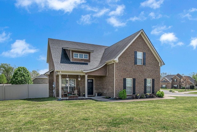 view of front facade with brick siding, roof with shingles, a front yard, and fence