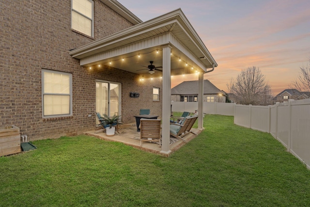 back of house at dusk with a ceiling fan, a fenced backyard, a yard, a patio, and brick siding