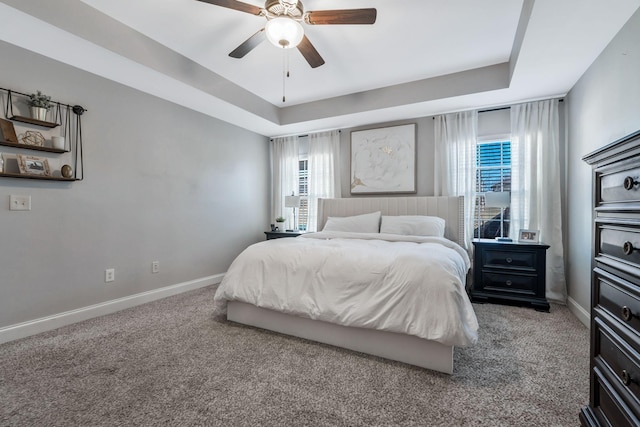 carpeted bedroom with a tray ceiling, baseboards, and multiple windows