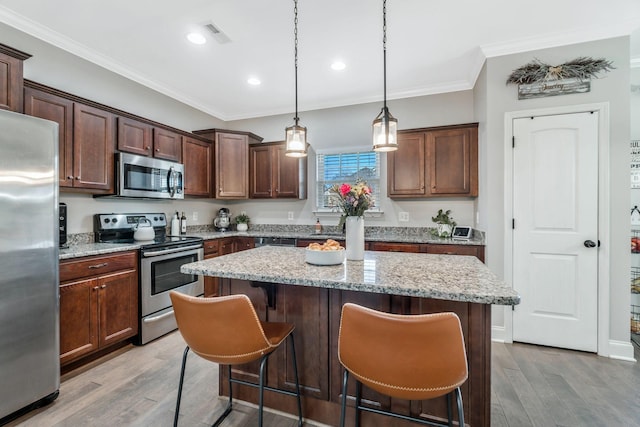 kitchen featuring a breakfast bar, crown molding, a center island, light wood-style flooring, and appliances with stainless steel finishes
