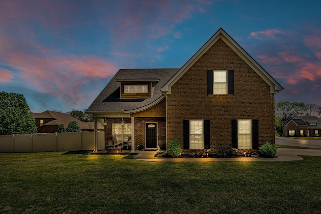view of front facade featuring fence, a lawn, and brick siding