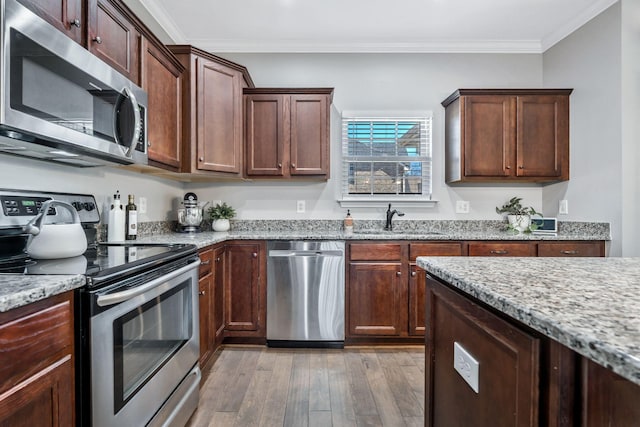 kitchen with light wood-style flooring, appliances with stainless steel finishes, light stone counters, and a sink