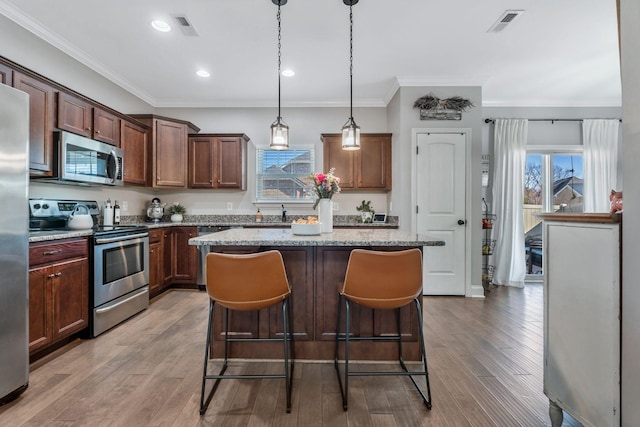 kitchen featuring crown molding, a kitchen island, appliances with stainless steel finishes, and a breakfast bar area