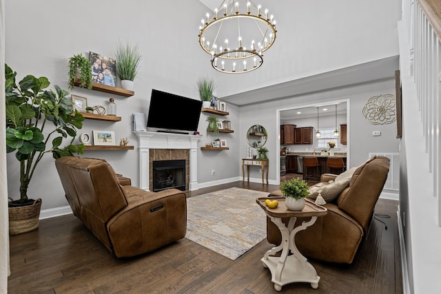 living room featuring a tiled fireplace, baseboards, an inviting chandelier, and dark wood-type flooring