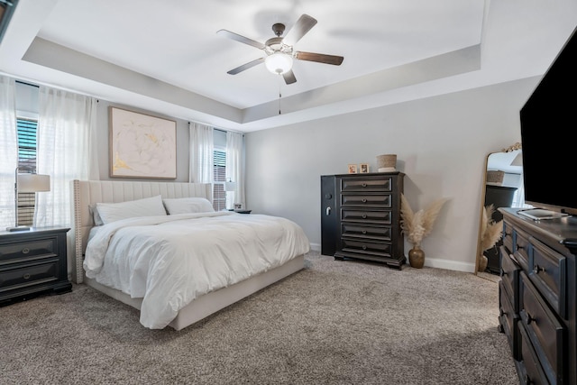 bedroom featuring a tray ceiling, carpet floors, baseboards, and ceiling fan