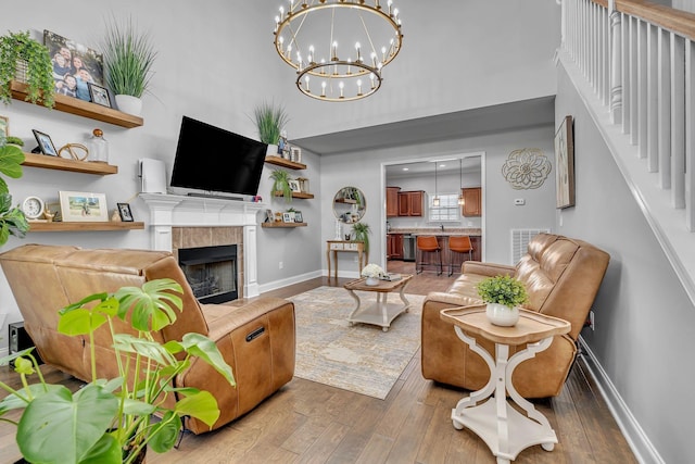 living room with a towering ceiling, baseboards, a chandelier, hardwood / wood-style floors, and a fireplace