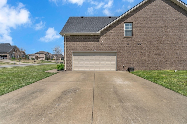 view of home's exterior featuring concrete driveway, a lawn, an attached garage, brick siding, and roof with shingles