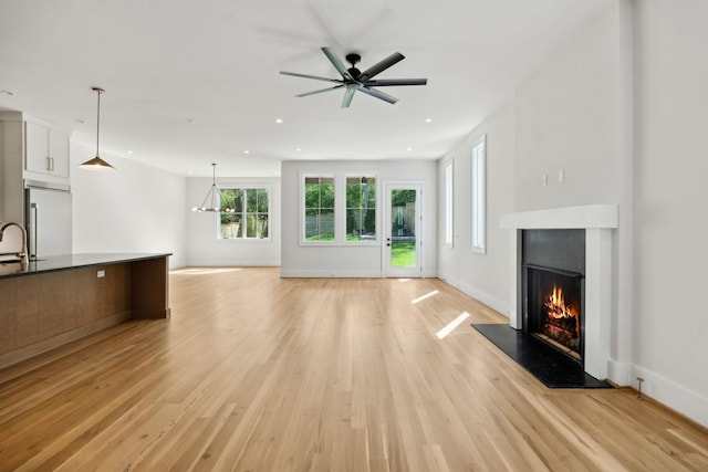 unfurnished living room featuring a ceiling fan, a sink, a warm lit fireplace, light wood-style flooring, and recessed lighting