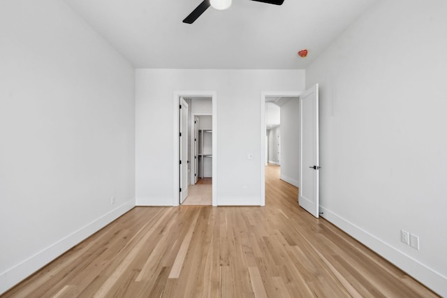 unfurnished bedroom with light wood-style flooring, a spacious closet, baseboards, and ceiling fan