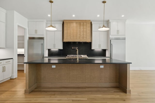 kitchen featuring built in refrigerator, high end refrigerator, dark countertops, a sink, and a kitchen island with sink