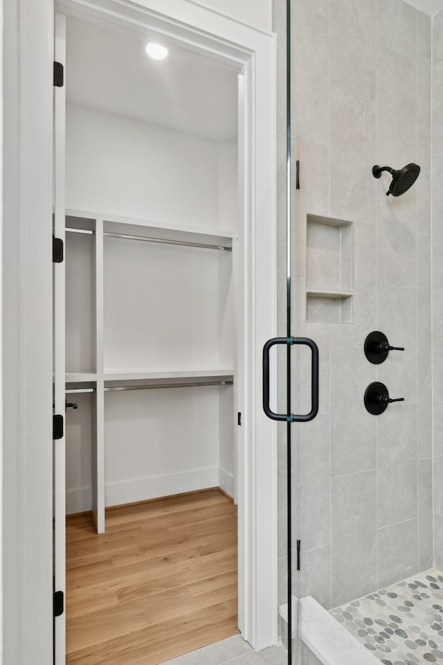 bathroom with a spacious closet, baseboards, wood finished floors, and a stall shower