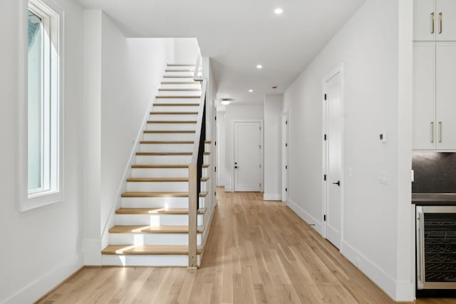 stairs with recessed lighting, wood finished floors, baseboards, and wine cooler