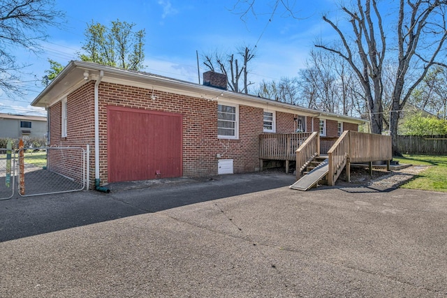 rear view of property with a wooden deck, brick siding, a chimney, and fence