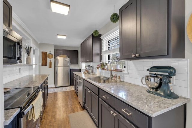 kitchen with wood finished floors, a sink, stainless steel appliances, backsplash, and light stone countertops