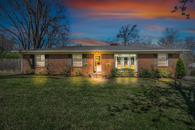 view of front of home featuring fence, a chimney, brick siding, and a yard
