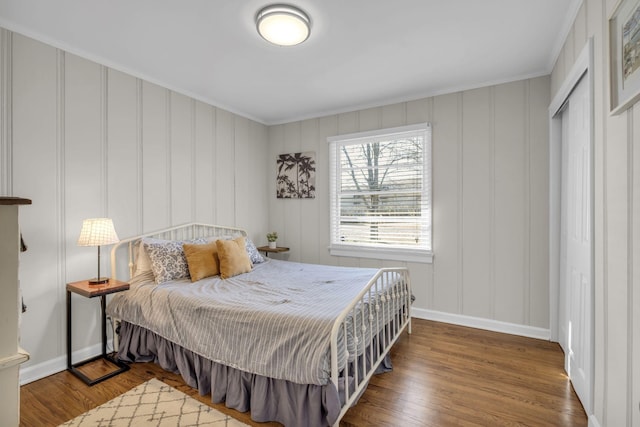 bedroom with wood finished floors, a decorative wall, baseboards, and ornamental molding