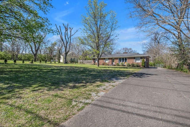 view of front of house with brick siding, aphalt driveway, fence, and a front yard