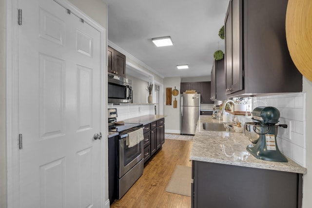 kitchen with light wood finished floors, stainless steel appliances, dark brown cabinets, a sink, and tasteful backsplash