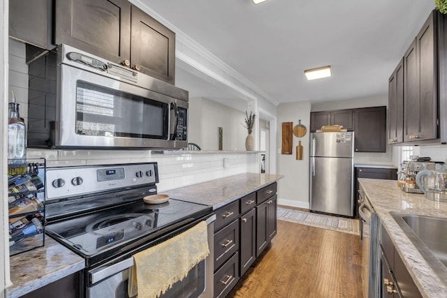 kitchen featuring light wood-type flooring, decorative backsplash, dark brown cabinetry, and appliances with stainless steel finishes