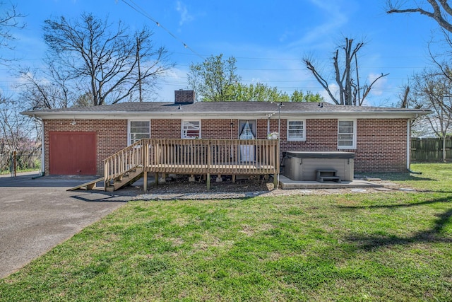 back of property with fence, a wooden deck, a lawn, brick siding, and a hot tub