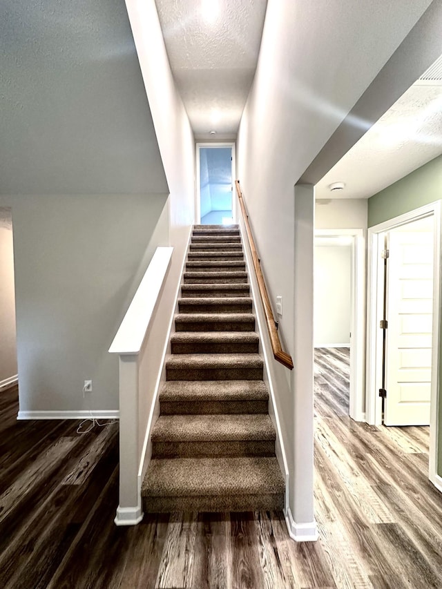 stairway featuring baseboards, wood finished floors, and a textured ceiling
