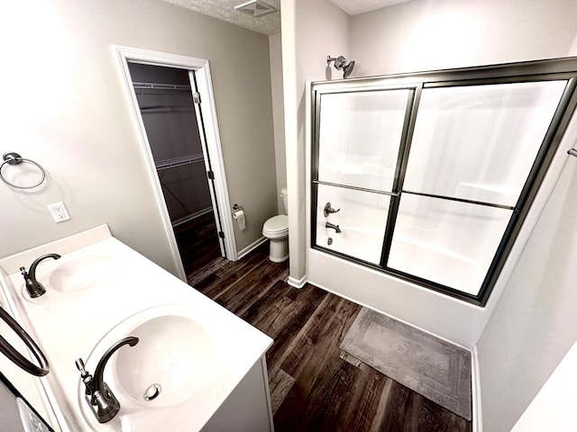 full bath with a sink, toilet, wood finished floors, combined bath / shower with glass door, and a walk in closet