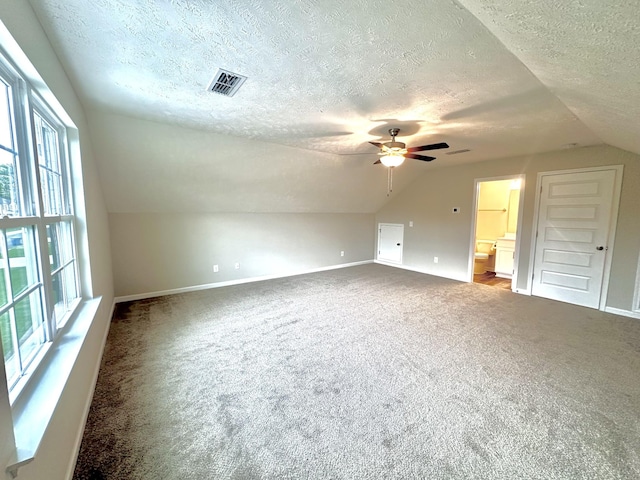 additional living space featuring a textured ceiling, ceiling fan, lofted ceiling, carpet flooring, and visible vents
