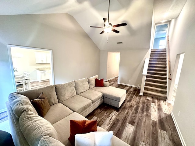 living area featuring dark wood finished floors, vaulted ceiling, visible vents, a ceiling fan, and stairs
