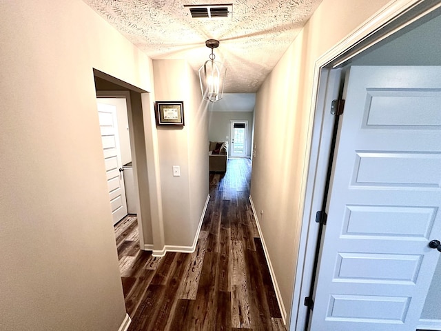 hallway with baseboards, visible vents, a textured ceiling, and dark wood-type flooring