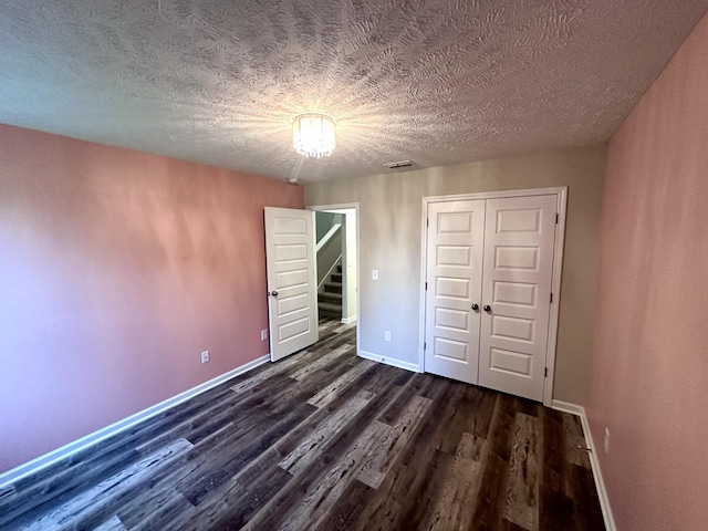 unfurnished bedroom with dark wood-style floors, a textured ceiling, a closet, baseboards, and visible vents