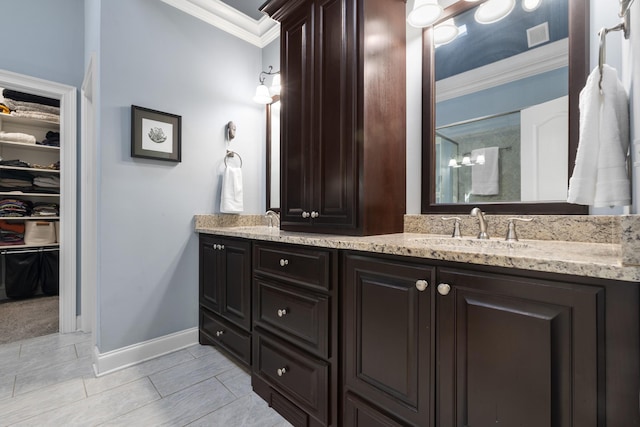 bathroom with double vanity, ornamental molding, a sink, baseboards, and a shower