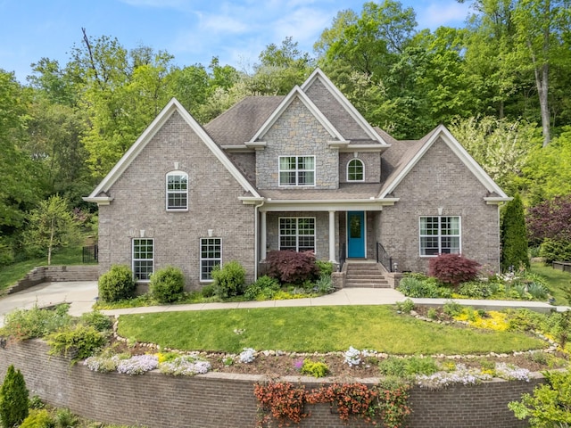craftsman inspired home with brick siding, a porch, a shingled roof, and a front yard