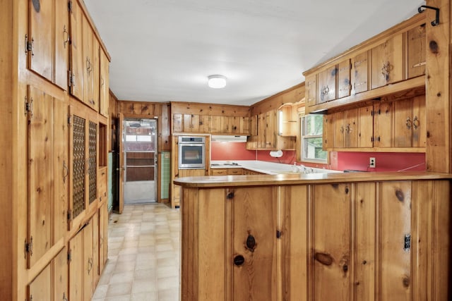 909 Hillsboro Rd, Franklin, TN 37064 - kitchen with brown cabinetry, oven, light floors, a peninsula, and under cabinet range hood