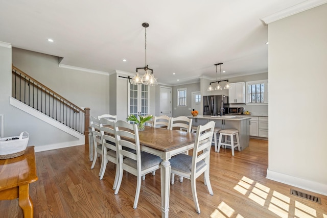 dining area featuring a chandelier, crown molding, light wood-style floors, recessed lighting, and stairs