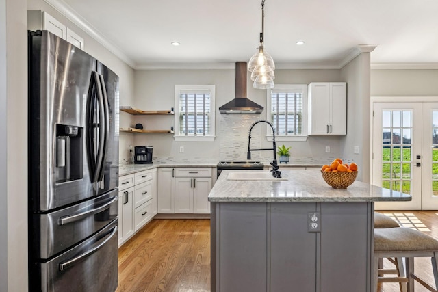 kitchen featuring stainless steel fridge, wall chimney range hood, light wood finished floors, a center island, and a kitchen bar