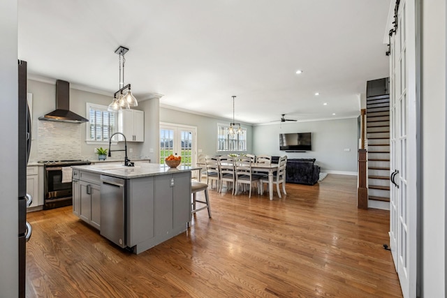 kitchen featuring wall chimney exhaust hood, stainless steel appliances, a sink, ornamental molding, and gray cabinets