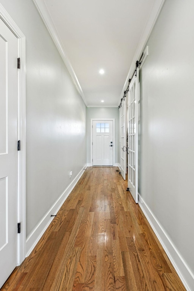 hallway with wood finished floors, baseboards, a barn door, and crown molding