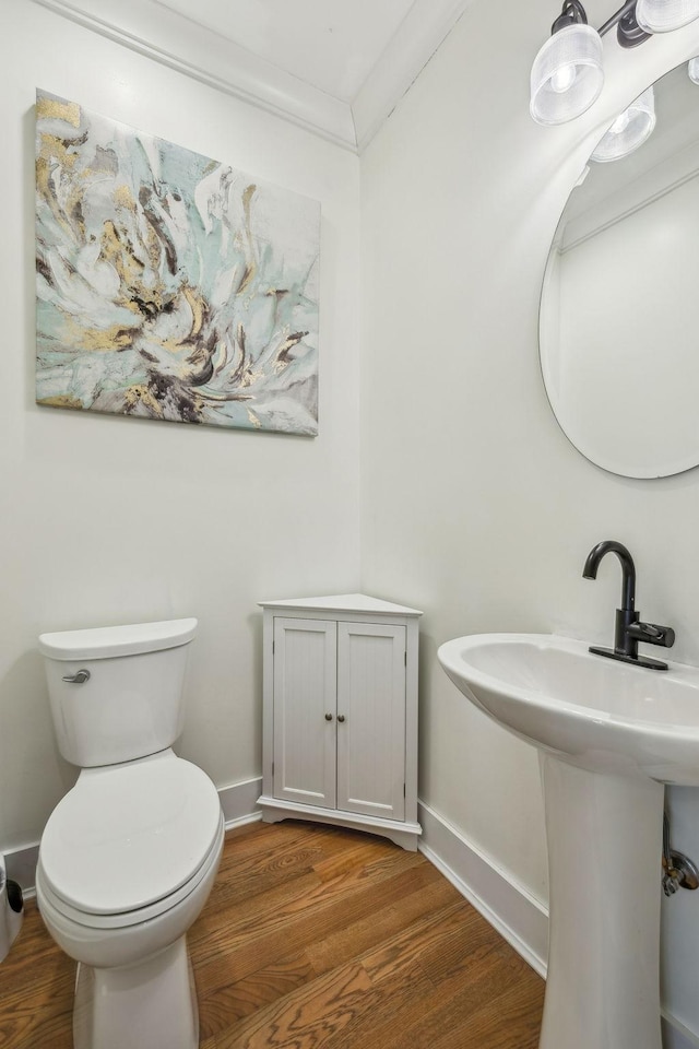 half bath featuring wood finished floors, toilet, baseboards, ornamental molding, and a sink