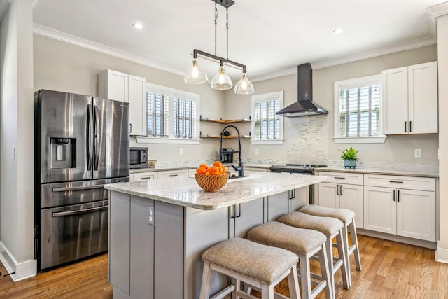 kitchen with appliances with stainless steel finishes, wall chimney exhaust hood, crown molding, an island with sink, and a breakfast bar