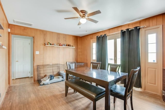 dining space featuring light wood-style floors, visible vents, a ceiling fan, and wood walls