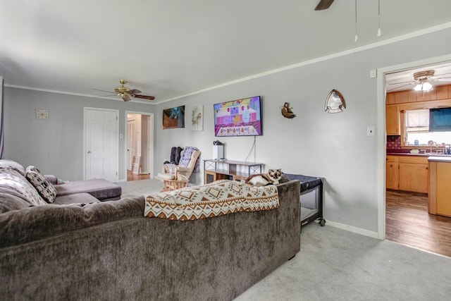 living area featuring light carpet, baseboards, ornamental molding, and ceiling fan