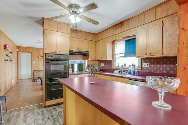 kitchen featuring light wood-style flooring, a sink, dobule oven black, ceiling fan, and wooden walls
