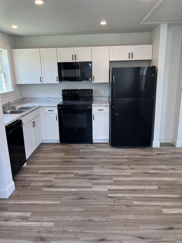 kitchen with white cabinets, light countertops, a sink, and black appliances